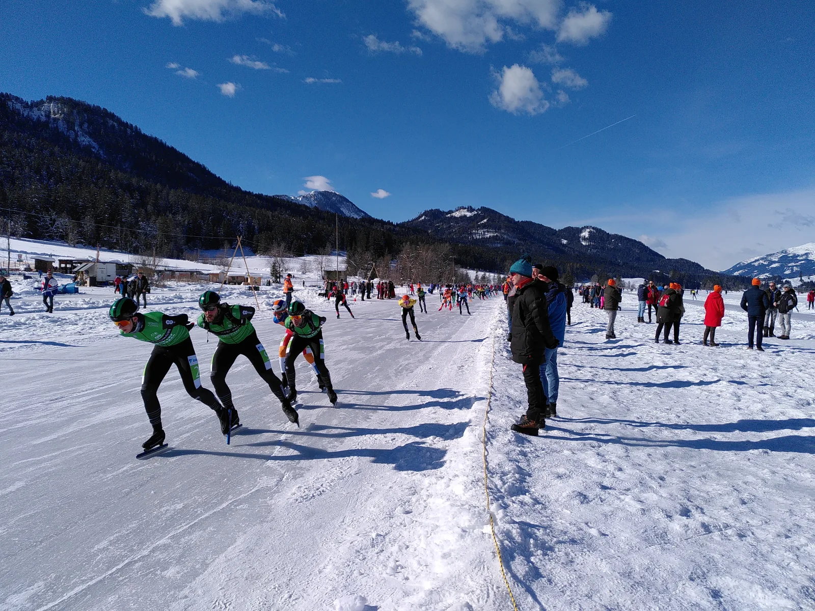 Schaatsers op natuurijs van de Weissensee in Karinthie tijdens de Alternatieve Elfstedentocht 2023 met besneeuwde bergen