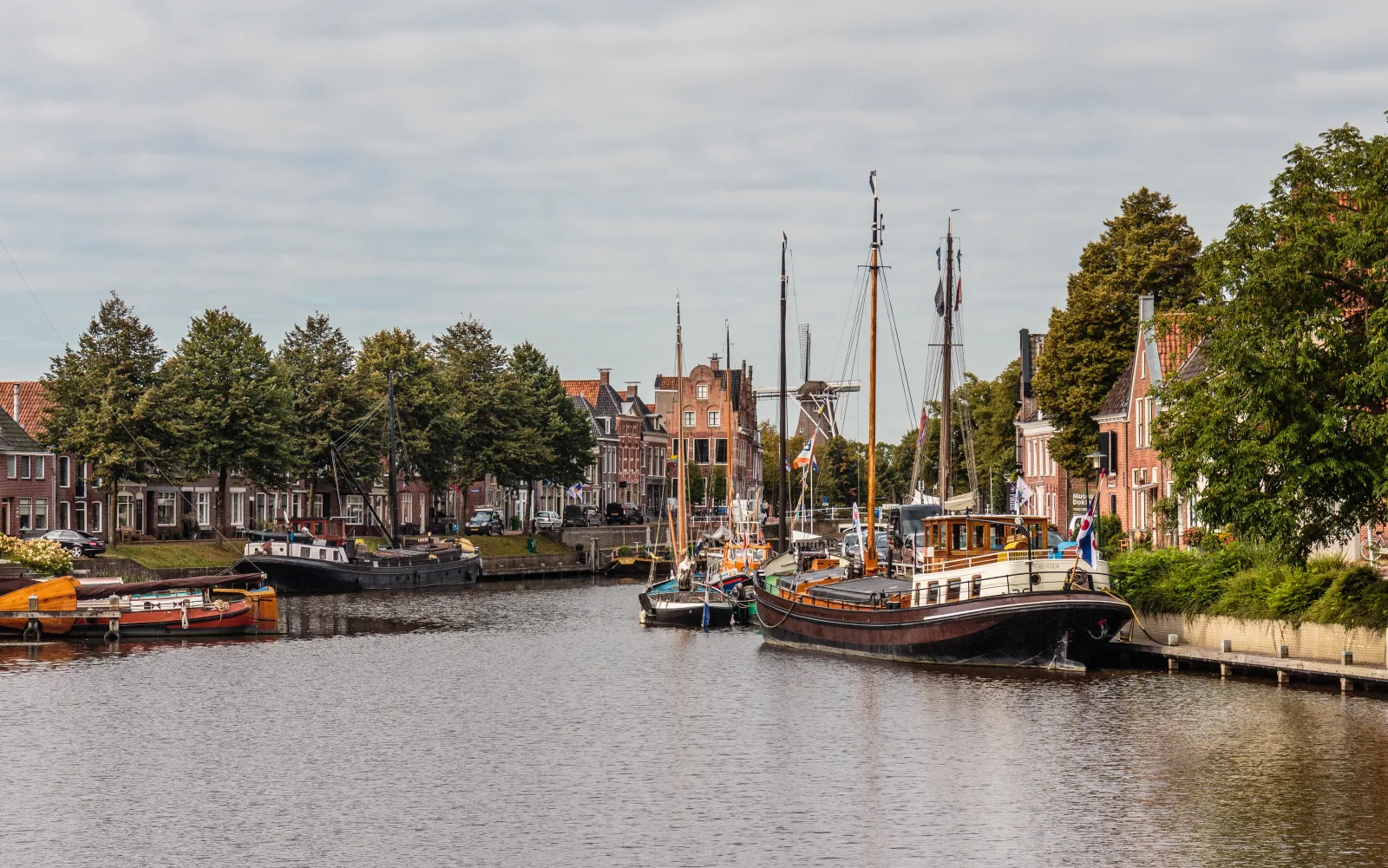 Het Grootdiep in Dokkum met historische zeilboten en oude pakhuizen langs de Friese gracht onder een wolkenlucht