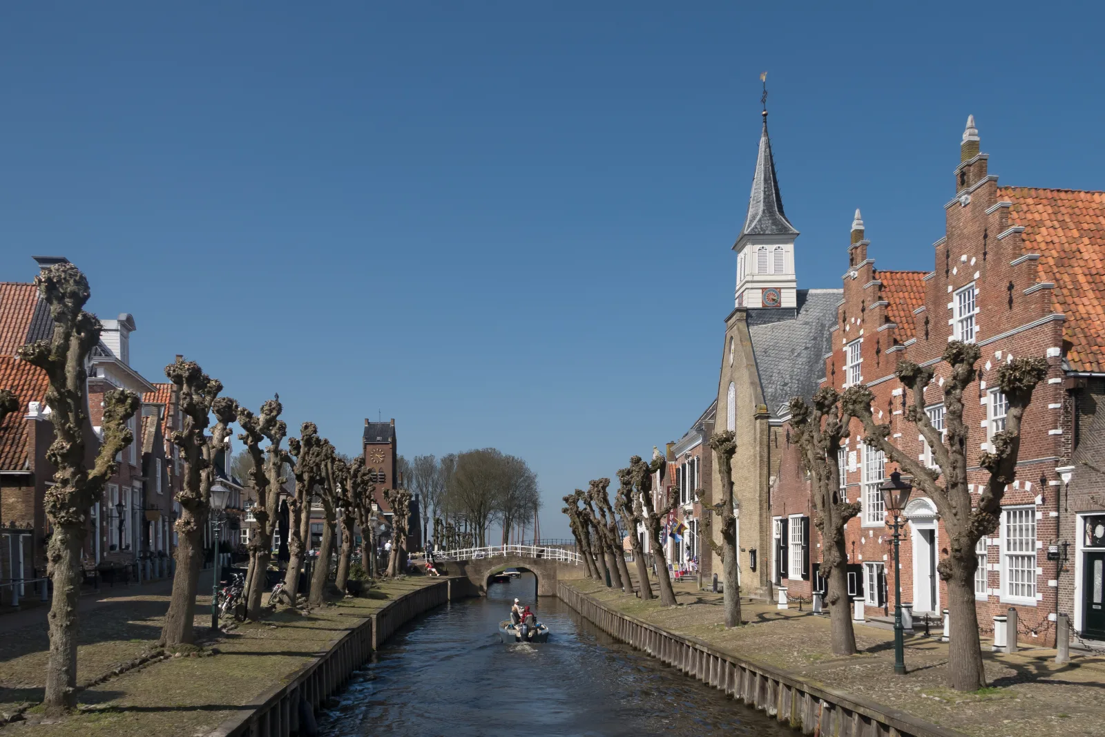 Stadsgracht van vestingstadje Sloten met geknotte lindebomen en de witte spits van de Hervormde kerk op de achtergrond