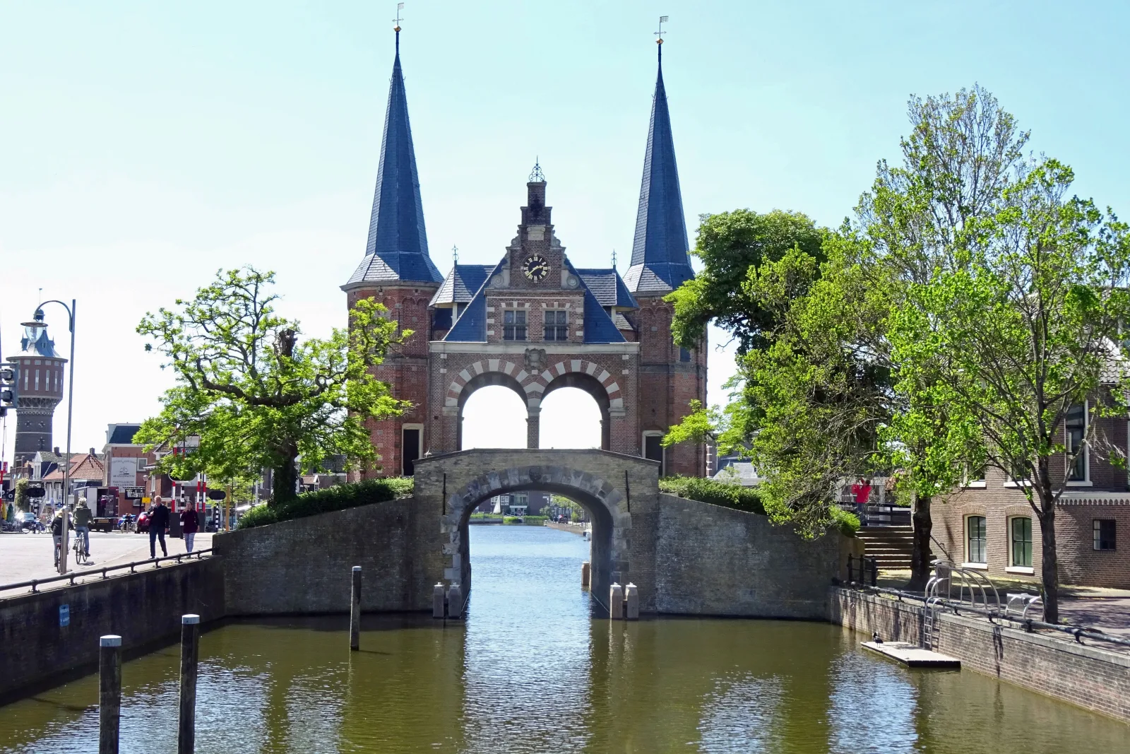 De iconische Waterpoort van Sneek met twee blauwe spitstorens, gespiegeld in het kalme water van de stadsgracht